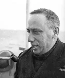 Informal head-and-shoulders portrait of man in dark coat and sweater, smoking a pipe