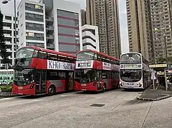 Three double-decker buses, two of them red, produced by Wrightbus at a bus stop in Hong Kong