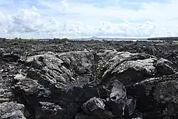 Volcanic landscape with lava flows and a lake in the background