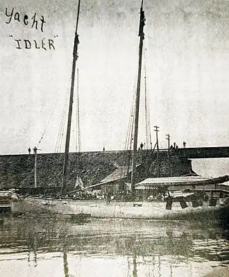 Black and white photograph of a 100-foot-long yacht, without sails, docked, with many people on deck