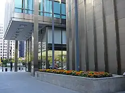 View of the facade as seen from ground level. The main building's upper stories, visible at left, overhang the recessed first and second floors. The mechanical tower is visible at right.