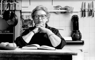 An elderly Grigson seated at a table in a kitchen