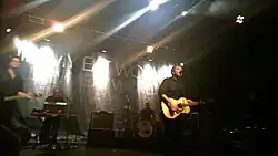 Several men performing onstage playing instruments and singing into a microphone