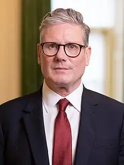 Head shot of Starmer wearing a dark suit jacket, white shirt, and red necktie