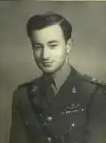 male in uniform tunic, collar and tie no headress on his leftbreast can be seem medal ribbons and SAS pattern parachute wings. He is also wearing a Sam Browne belt