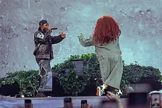 SZA and Lamar performing onstage in front of a black car surrounded by leaves