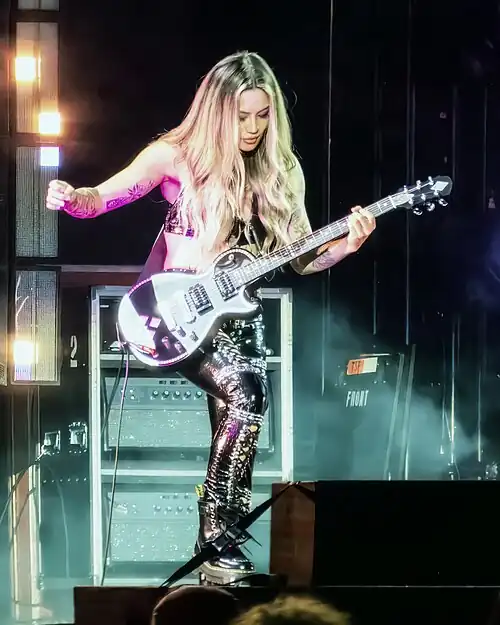 Kiki Wong playing guitar on stage, with her foot on an effects pedal.