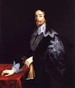 Oil painting of King Charles I of England. In his left hand he holds a pair of leather gloves. He is wearing a dark blue velvet cape, the left shoulder bearing a large white star with the red cross of St George in the middle. His face is very angular with a long chin accompanied by a wispy moustache and goatee and long curly hair falling over a white lace collar.