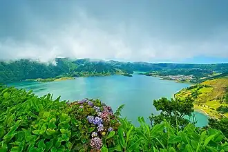 Photo of a bright blue lake, taken from above. The lake is surrounded by green hills.