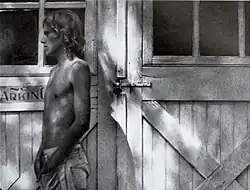 graphite drawing of a thin young light haired man drawn in intense values, photo-like quality. He has gently curled, long hair, wearing only jeans.