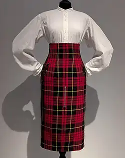 High-waisted tartan skirt worn over long-sleeved button-up white shirt