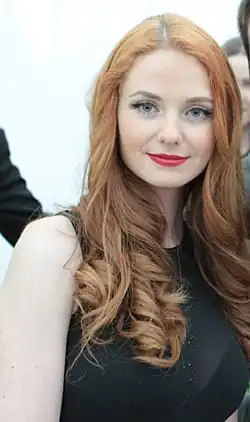 close-up of Lena Katina wearing a sheer, black, sleeveless top revealing a black bra, smiling directly at camera