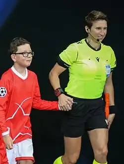 some football referees lead some mascots through a tunnel at a big club football match