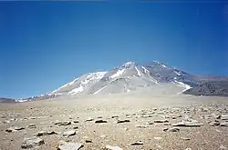 A white-grey mountain with snow patches rises above a rock-covered terrain
