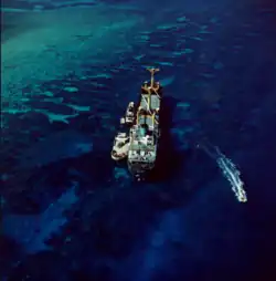 Aerial view of a ship aground on a coral reef with tugboats on her left side
