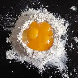 Eggs are cracked into a well of flour.