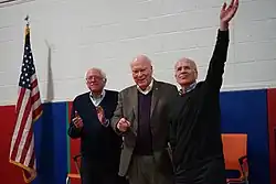 Three older men on a stage next to an American flag. (from Vermont)
