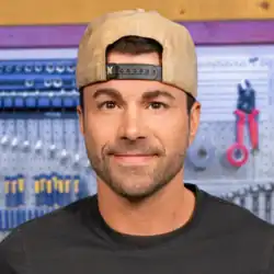 Headshot of Mark Rober in front of his workbench. He is a white man with short dark and a stubble beard, wearing a light backwards cap and a black T-shirt.