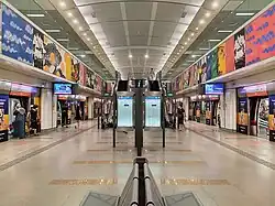 The island platform of Buangkok station featuring a line map and benches, with the station artwork adorned above the platform screen doors. At the centre of the image, escalators, and stairs lead to the upper level of the concourse.