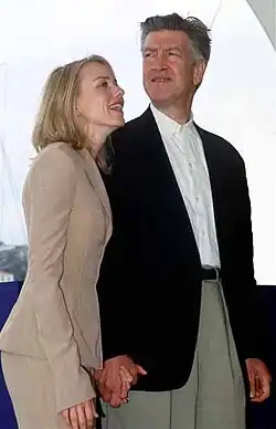 A blonde woman and a grey-haired man, holding hands and smiling
