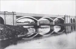 A black and white photo of a three-arch viaduct crossing a river, with abutments on each side.