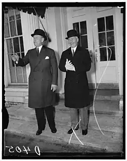 Two well-dressed men in suits and hats stand on outside a building