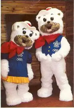 Two polar bear mascots with fuzzy white fur. The female is wearing a blue dress, and the male a blue vest. They each wear a red bandana and cowboy hat.