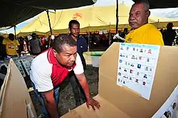 Man at a cardboard booth with pictures of political candidates attached to one wall