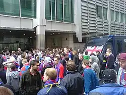 A crowd of people and a police van outside a building.