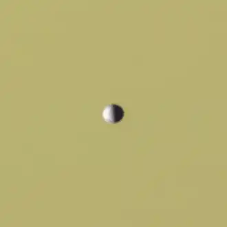A small, half-illuminated ellipsoidal object in front of Saturn as a backdrop