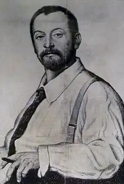 A man with a cropped beard and short hair in a shirt and tie with suspenders holding a pen