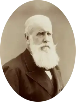 Half-length photographic portrait of an older man with white hair and beard dressed in a dark jacket and necktie