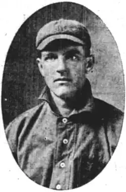 A man wearing a dark baseball jersey with a high collar and a cap.
