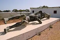 Colour photograph of two patinaed bronze statues on a plinth in an open-air museum enclosure.