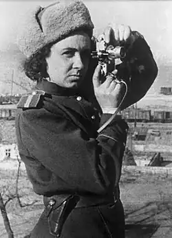 Lander in Red Army uniform, facing the viewer with a camera to her eye, ready to take a photograph.