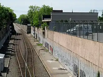 Disused platforms next to an active railway line in a cut, with a one-story midcentury building at right