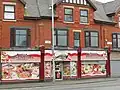 A Polish shop in Harpurhey incorporating the typical aesthetic of red and white, garish window vinyls, and a vintage image of a traditional spiżarnia on its shopfront