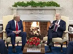 The Oval Office Swedish ivy prominently visible on the mantle, with a bright green appearance stretching across the entire mantle. There is a fire beneath it as Joe Biden (right) and Donald Trump (left) sit in front of it, facing away from it.