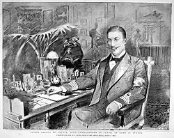 George, a well-built young man with a waxed moustache, sits in a well-appointed room wearing a naval officer's mess dress