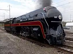 A black streamlined steam locomotive with overhead lines in the background