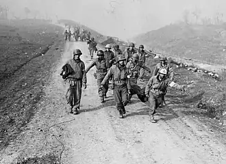Monochrome photo of soldiers carrying wounded people on a long dirt road