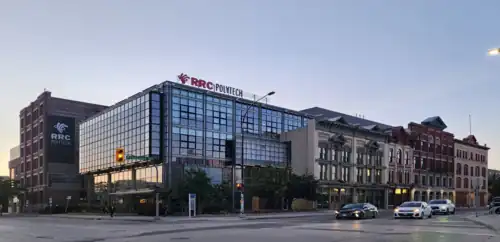 A cluster of attached buildings with signage atop that says RRC Polytech. The left-most building is glass and steel, but further right are several building facades in a much older style, in brick and stonework.