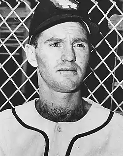 A man in a white baseball uniform and dark cap.