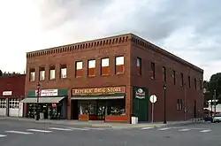 Two-story red brick building on a downtown street corner with green and red storefront signage
