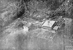 Black and white aerial photo of a multi-story building with a tall mast next to it. Smoke is visible in the air in front of the building.