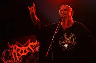 Jiří Valter wearing a black t-shirt with Satanic print, standing onstage, singing into a microphone