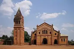 Photograph depicting the Catholic parish church in Rwamagana, Eastern Province, including the main entrance, façade, the separate bell tower, and dirt forecourt