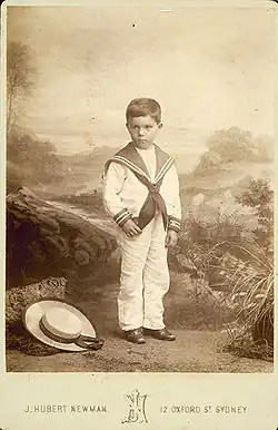 Photograph of a boy on Oxford Street, Sydney, Australia, wearing a sailor suit, with a sennit straw hat at his feet
