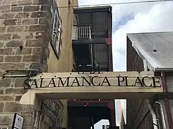 Two metallic words in black set on a frame, suspended between two buildings.