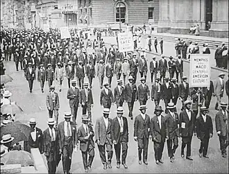 A large group of people, wearing suits, marching in an orderly fashion down a wide street